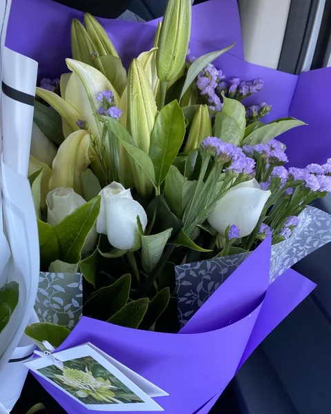 White lilies, white roses and purple statice in violet wrap
